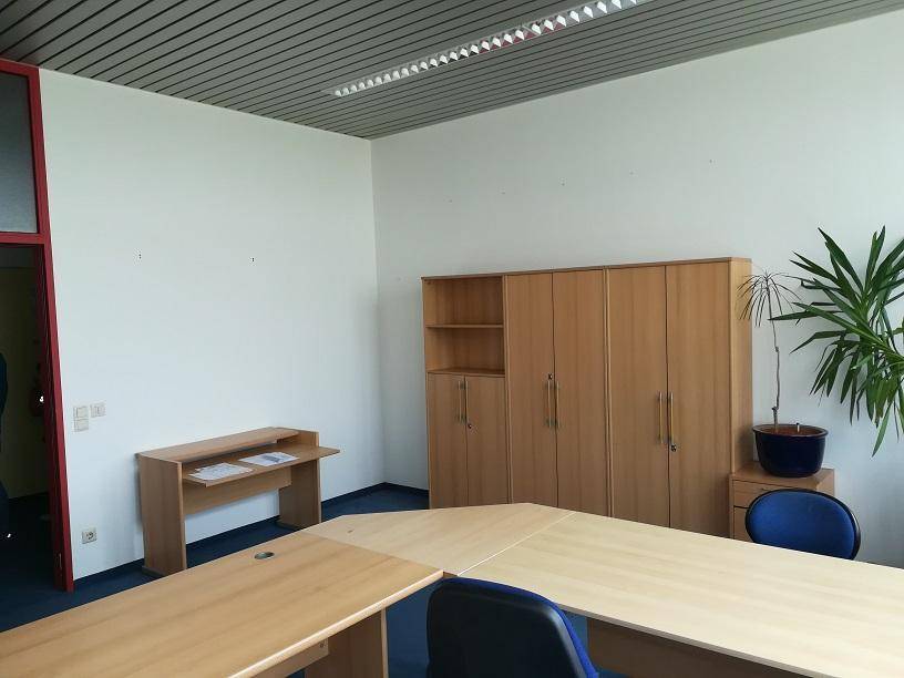 Möbliertes Büro mit hellen Holzmöbeln, einem Schrank und einem Schreibtisch, sowie einer Zimmerpflanze.