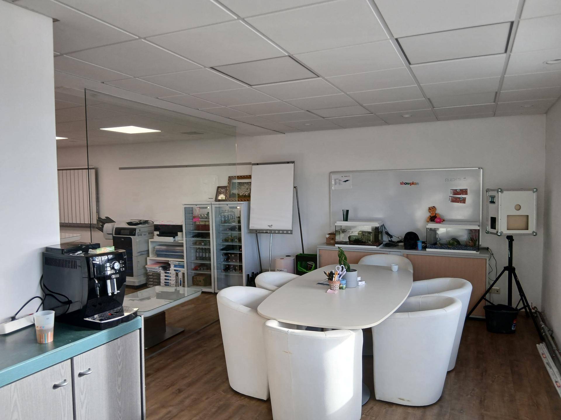 Besprechungsbereich im Büro mit ovalem Tisch, weißen Stühlen und einer Kaffeemaschine.