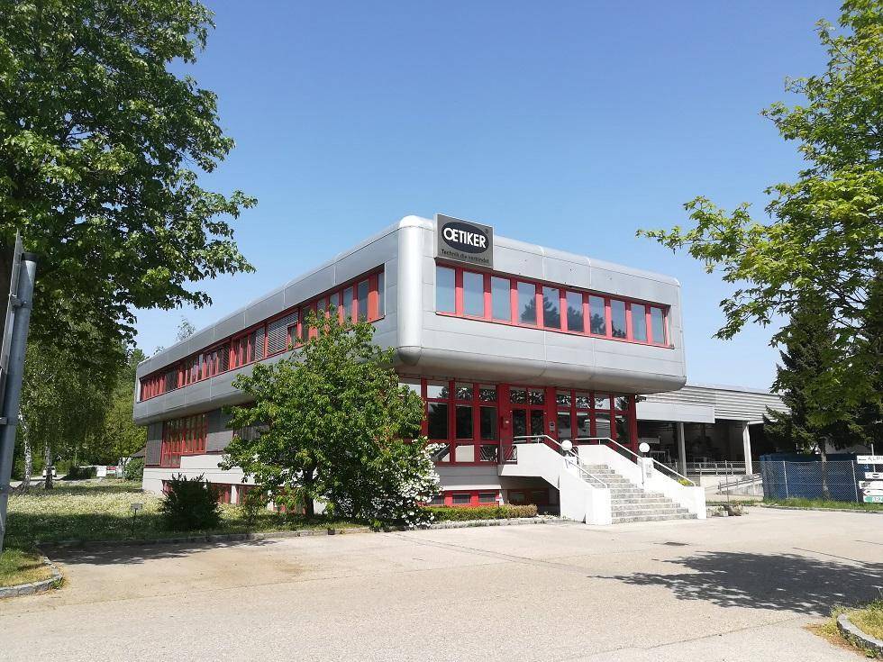 Modernes Geschäftsgebäude mit markanter Architektur, roten Fensterrahmen und umgebender Grünfläche.