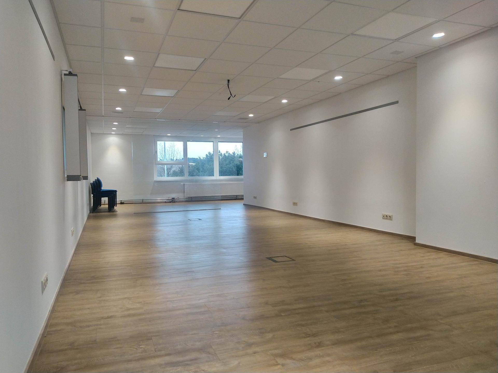 Leerer, heller Büroraum mit Laminatboden, weißen Wänden und abgehängter Decke.
