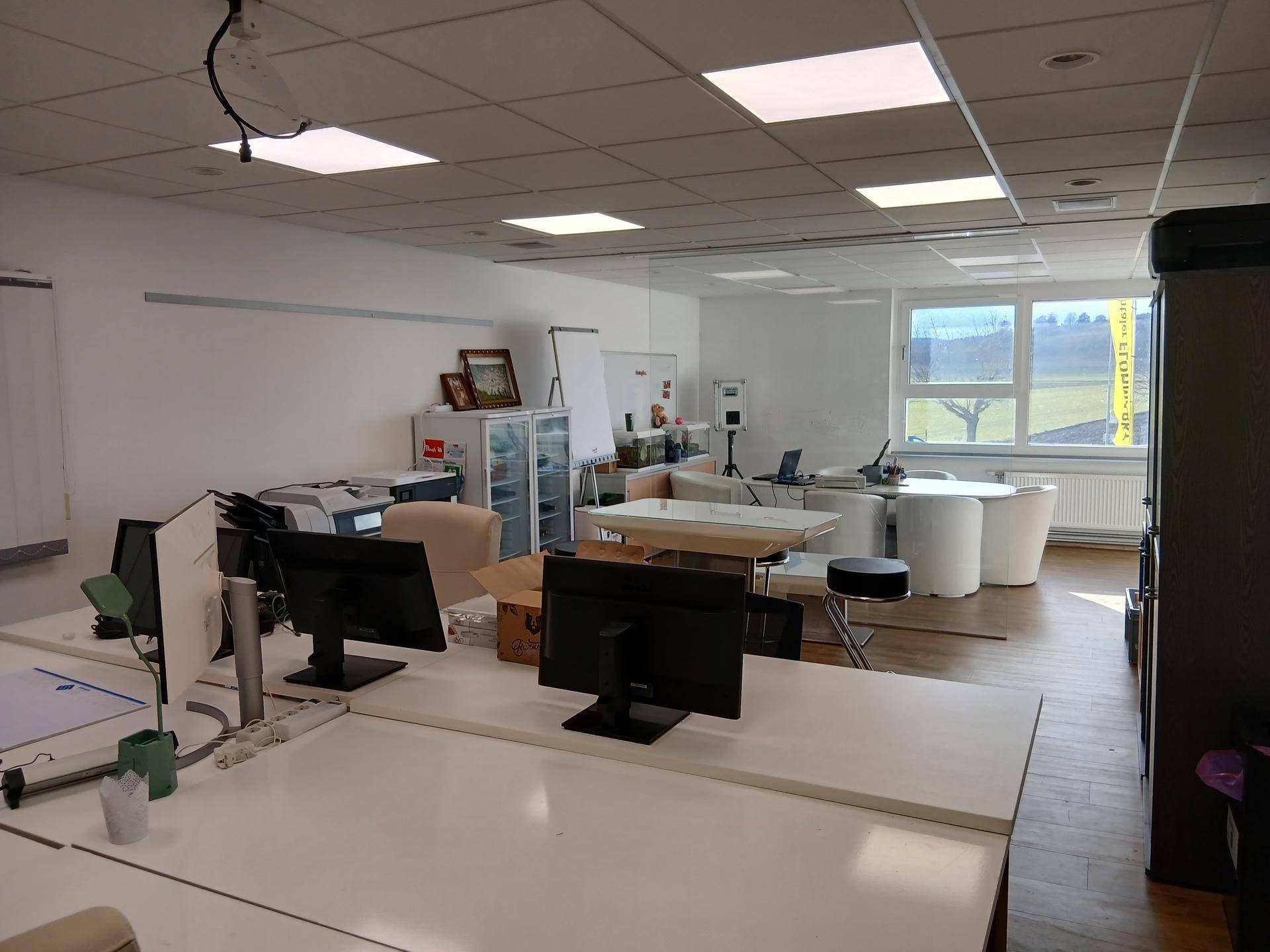Helles Büro mit Arbeitsplätzen, Besprechungstisch und weitem Blick auf Felder und Landschaft.
