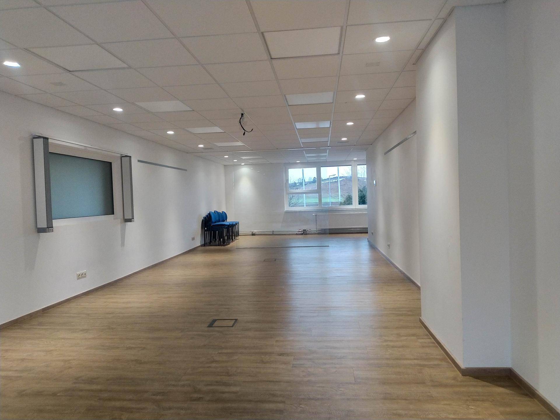 Großer, leerer Büroraum mit Laminatboden, weißen Wänden und Fenstern mit Blick ins Freie.