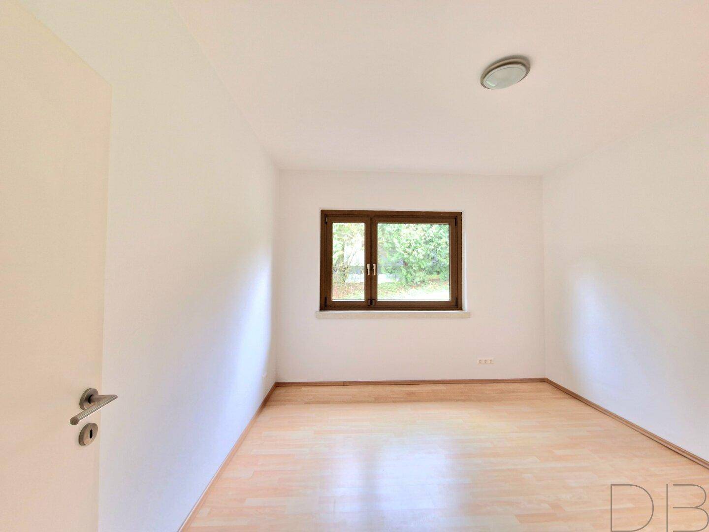 Helles, leeres Zimmer mit Holzboden und Fenster, ideal als Schlaf- oder Arbeitszimmer.