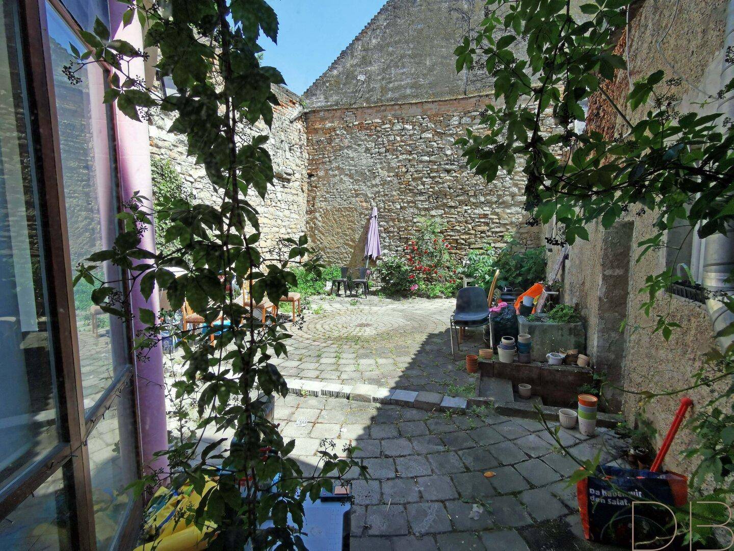 Idyllischer, gepflasterter Innenhof mit üppigem Grün und alten Steinmauern, bietet eine ruhige Oase.