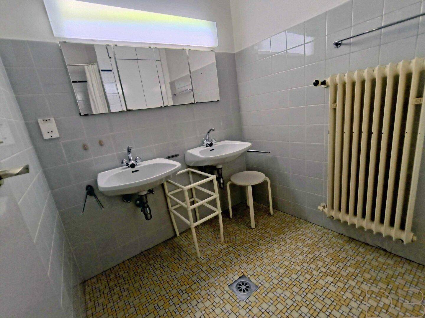 Badezimmer mit zwei Waschbecken, hellblauen Fliesen und Heizkörper.