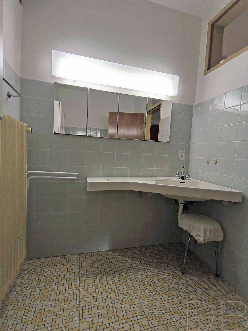 Badezimmer mit barrierefreiem Waschbecken, hellblauen Fliesen und Spiegelschrank.