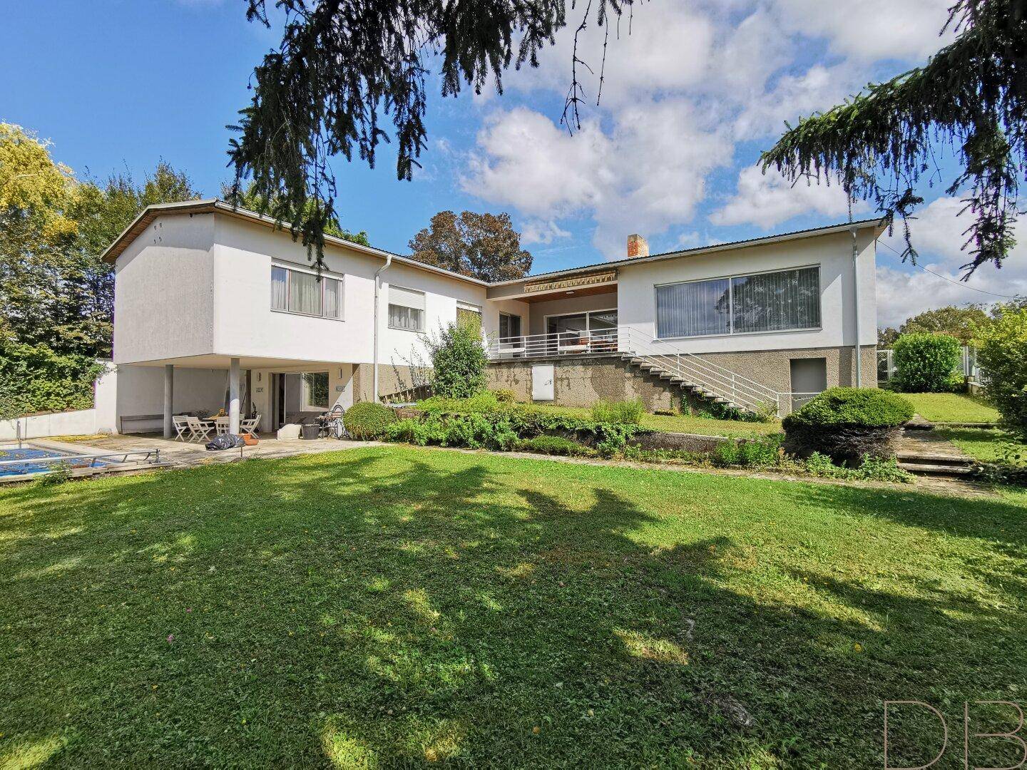 Weitläufiger Gartenbereich mit Rasen, altem Baumbestand und Blick auf die Hausfassade mit Terrasse.