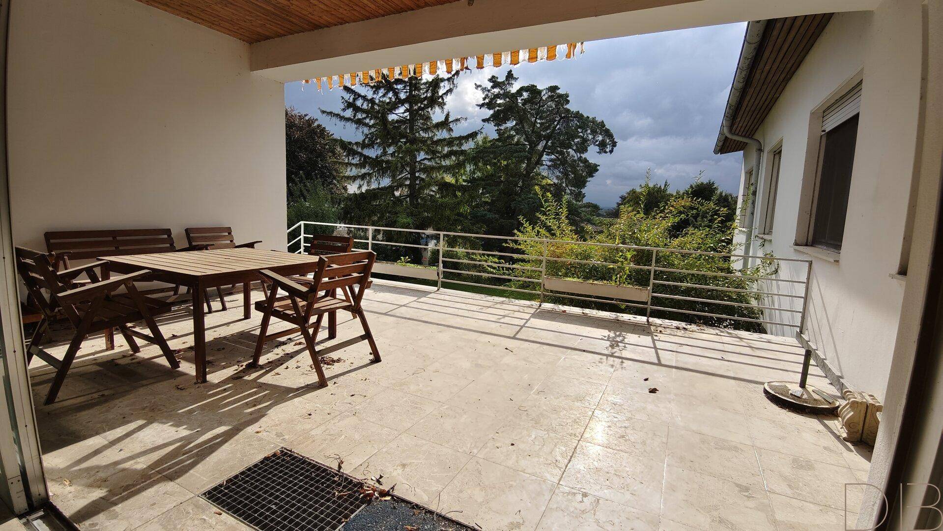 Überdachte Terrasse mit Holztisch und Stühlen, ideal für Mahlzeiten im Freien.