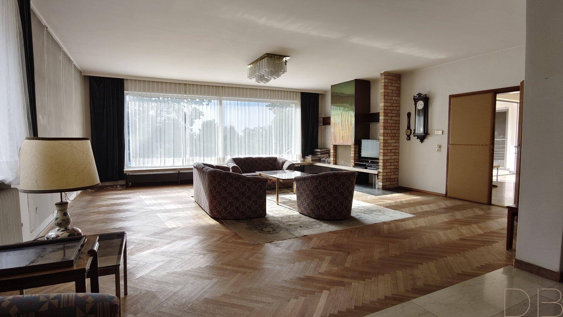 Großes Wohnzimmer mit Fischgrätparkett, Kamin und Blick ins Grüne.