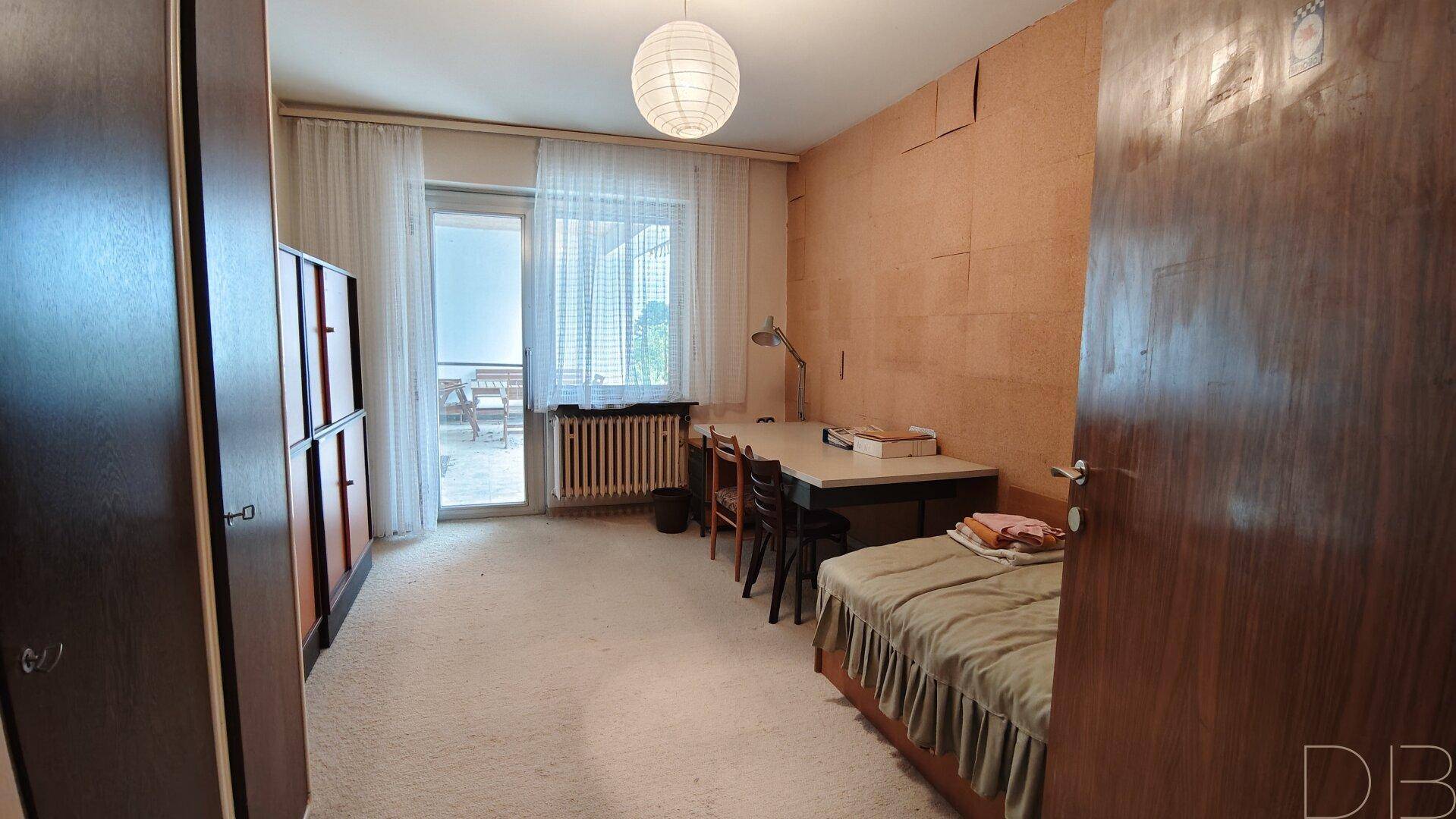 Schlafzimmer mit Teppichboden, Schreibtisch und Zugang zur Terrasse.