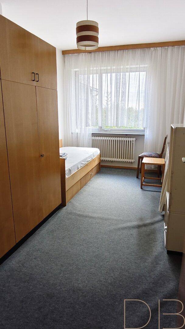 Schlafzimmer mit Teppichboden, Einbauschrank und großem Fenster.