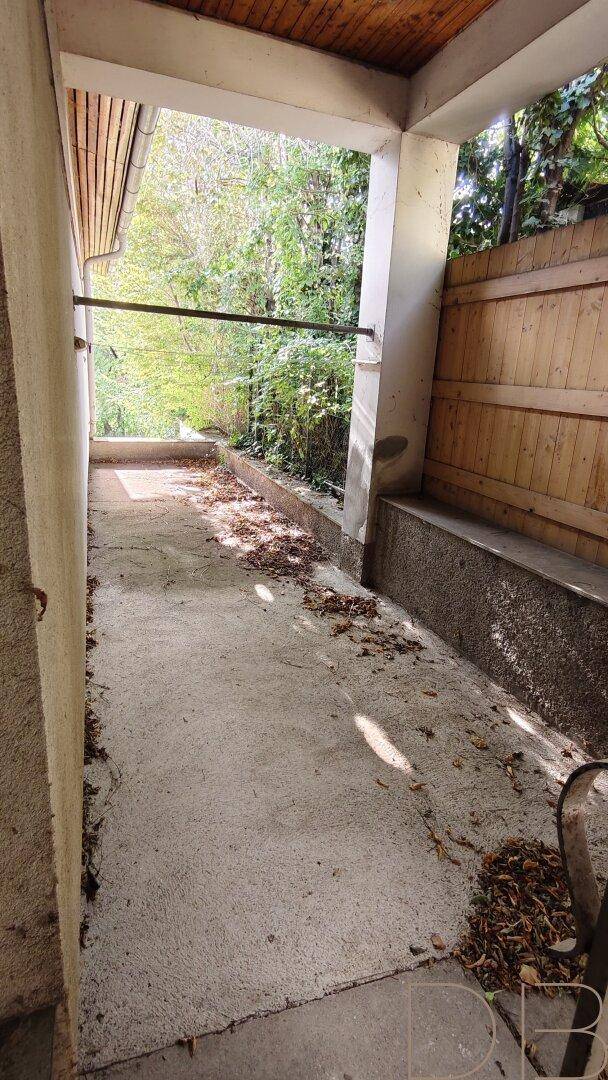 Überdachter Gang mit Betonboden und Blick ins Grüne, ideal als geschützter Außenbereich.