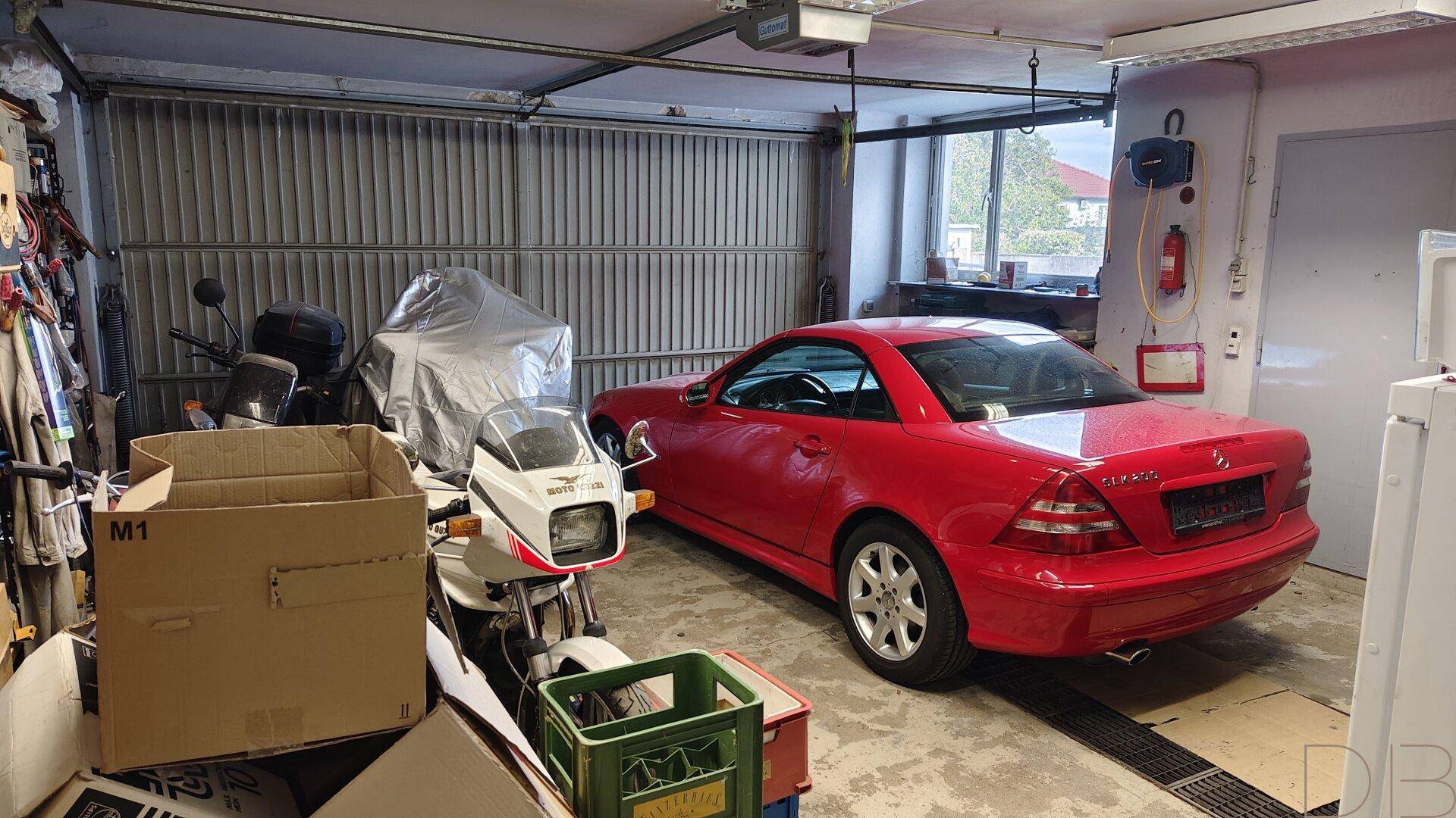 Geräumige Garage mit rotem Sportwagen, Motorrädern und Stauraum.