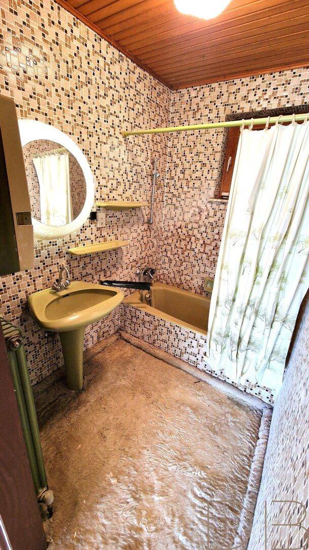Badezimmer mit kleinen Mosaikfliesen, grüner Badewanne und Waschbecken im 80er-Jahre-Stil.