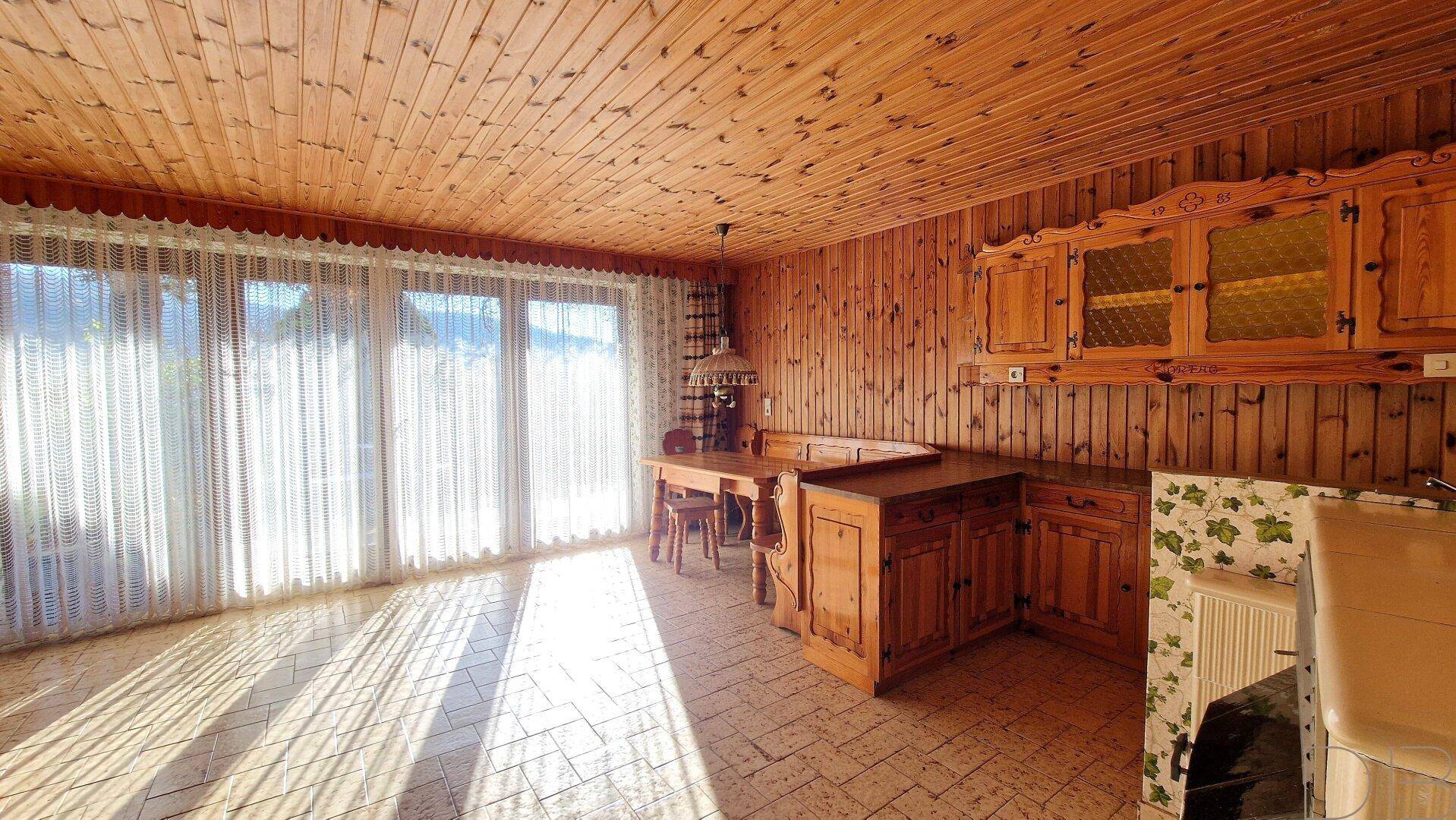 Rustikale Wohnküche mit Holzvertäfelung, Essbereich und großen Fenstern zum Garten.