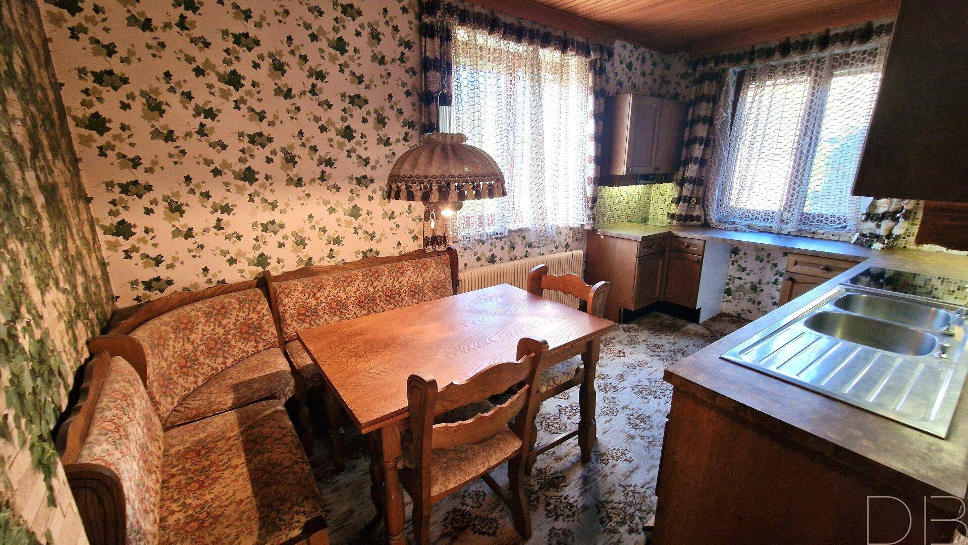 Kleine Küche mit Essnische, floraler Tapete und traditionellen Holzschränken.