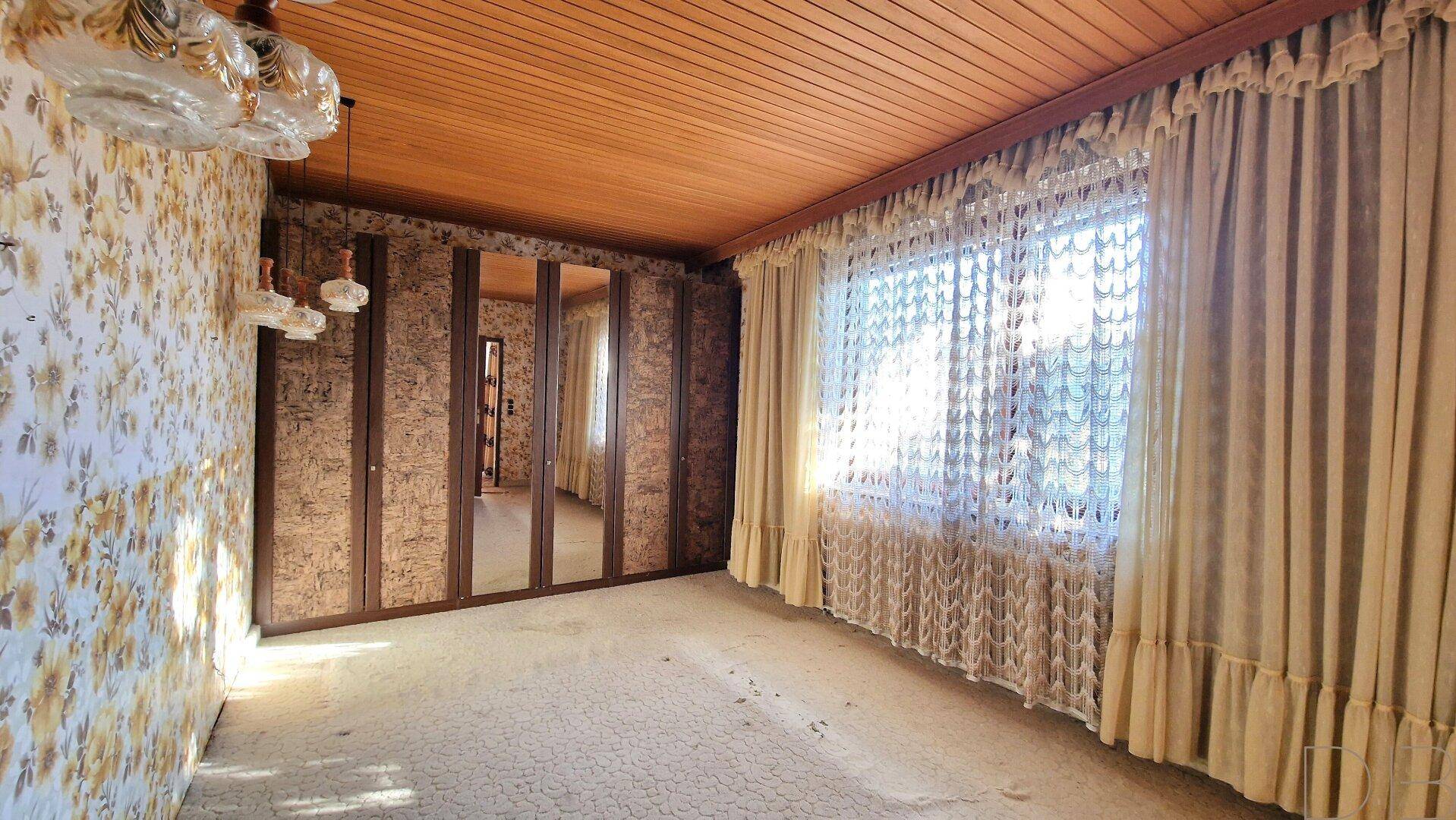 Schlafzimmer mit Teppichboden, Holzdecke und einem großen Spiegelschrank.