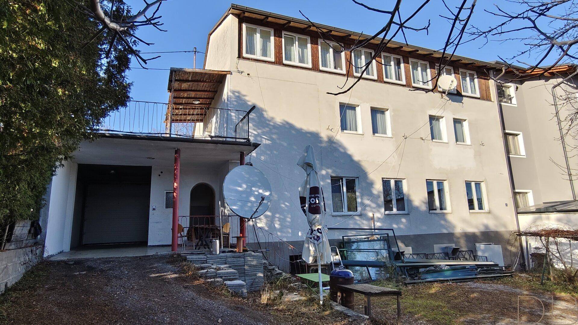 Ansicht der Gebäudefassade mit Balkon, Garage und umliegendem Grundstück.