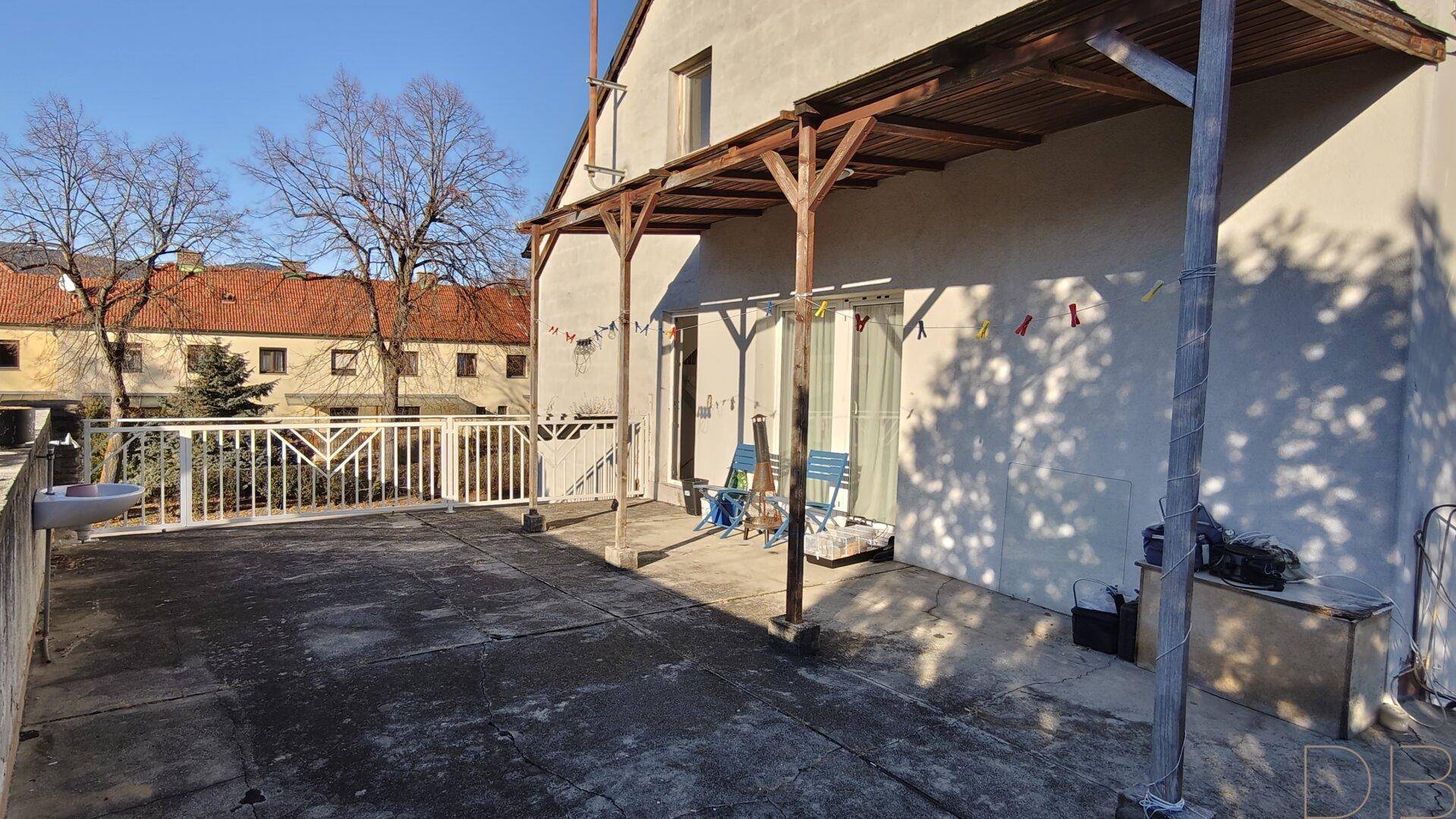 Weitläufige Terrasse mit Überdachung und Zugang zum Gebäude, bietet viel Platz im Freien.