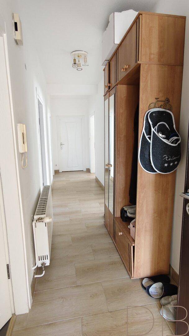 Langer Flur mit Holzschrank und hellem Laminatboden, der zu weiteren Räumen führt.