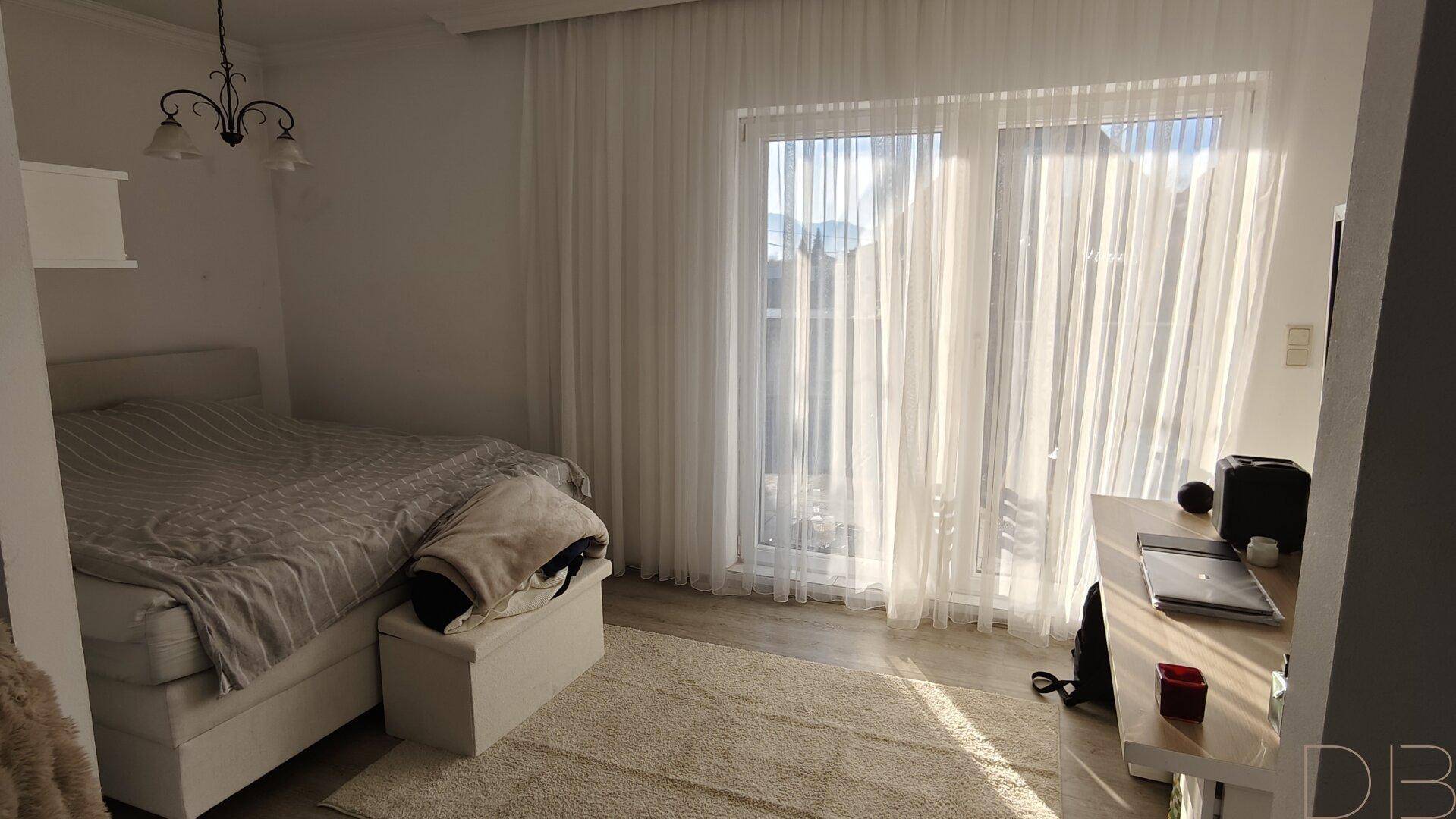 Helles Schlafzimmer mit Doppelbett und großen Fenstern, die viel Sonnenlicht hereinlassen.