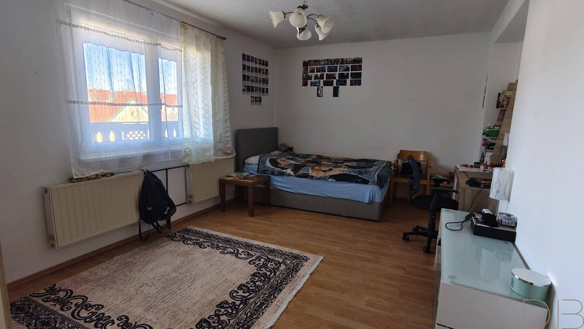 Helles Schlafzimmer mit Bett, Schreibtisch und Teppich auf Laminatboden.