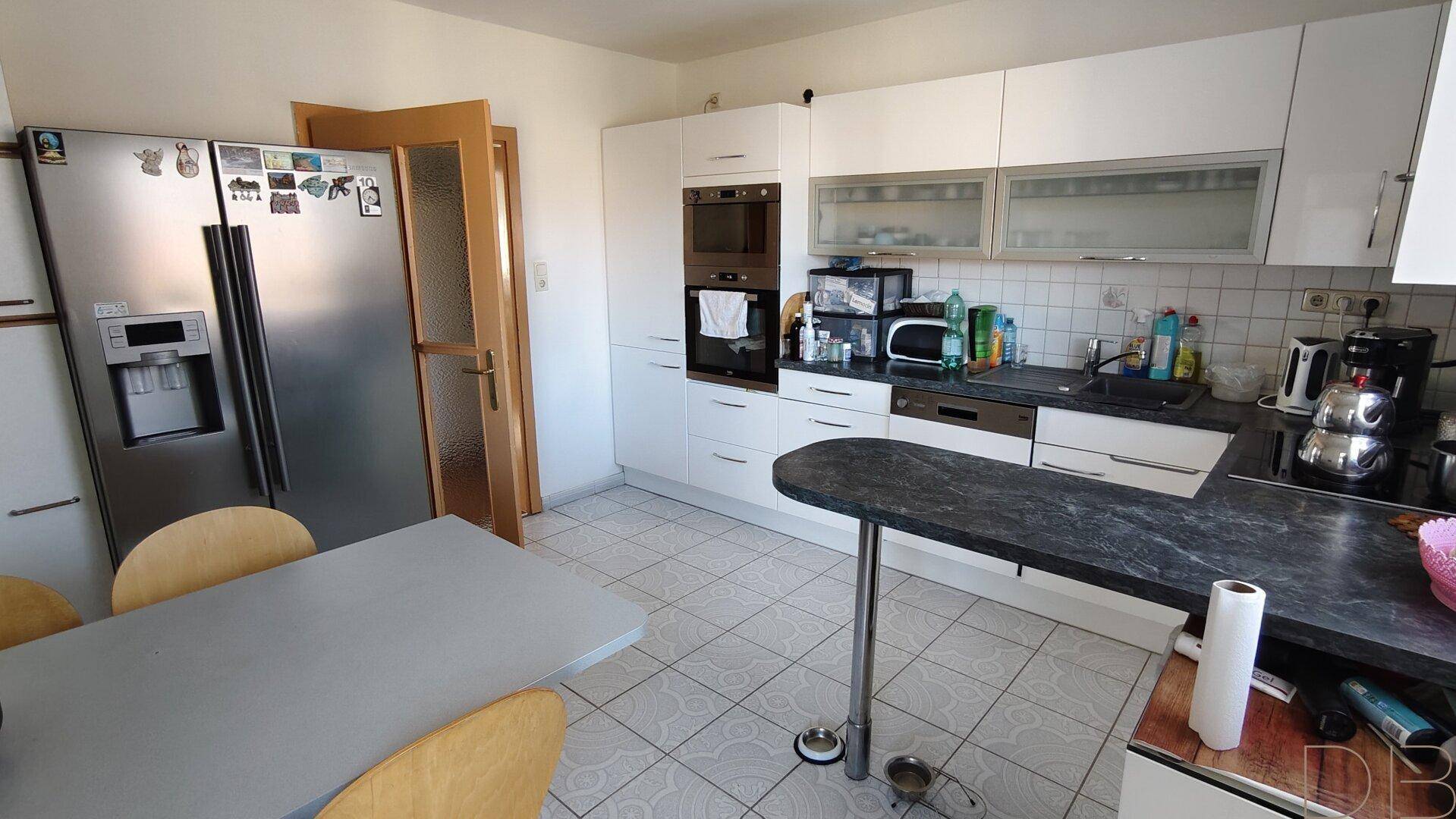 Helle Küche mit weißen Schränken, großem Kühlschrank und Essbereich, funktional und geräumig.