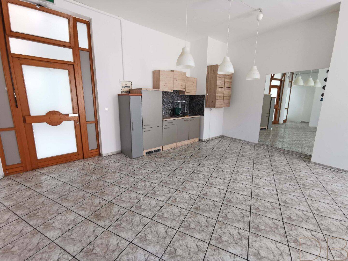 Heller Gewerberaum mit funktionaler Küchenzeile, Fliesenboden und großen Fenstertüren.