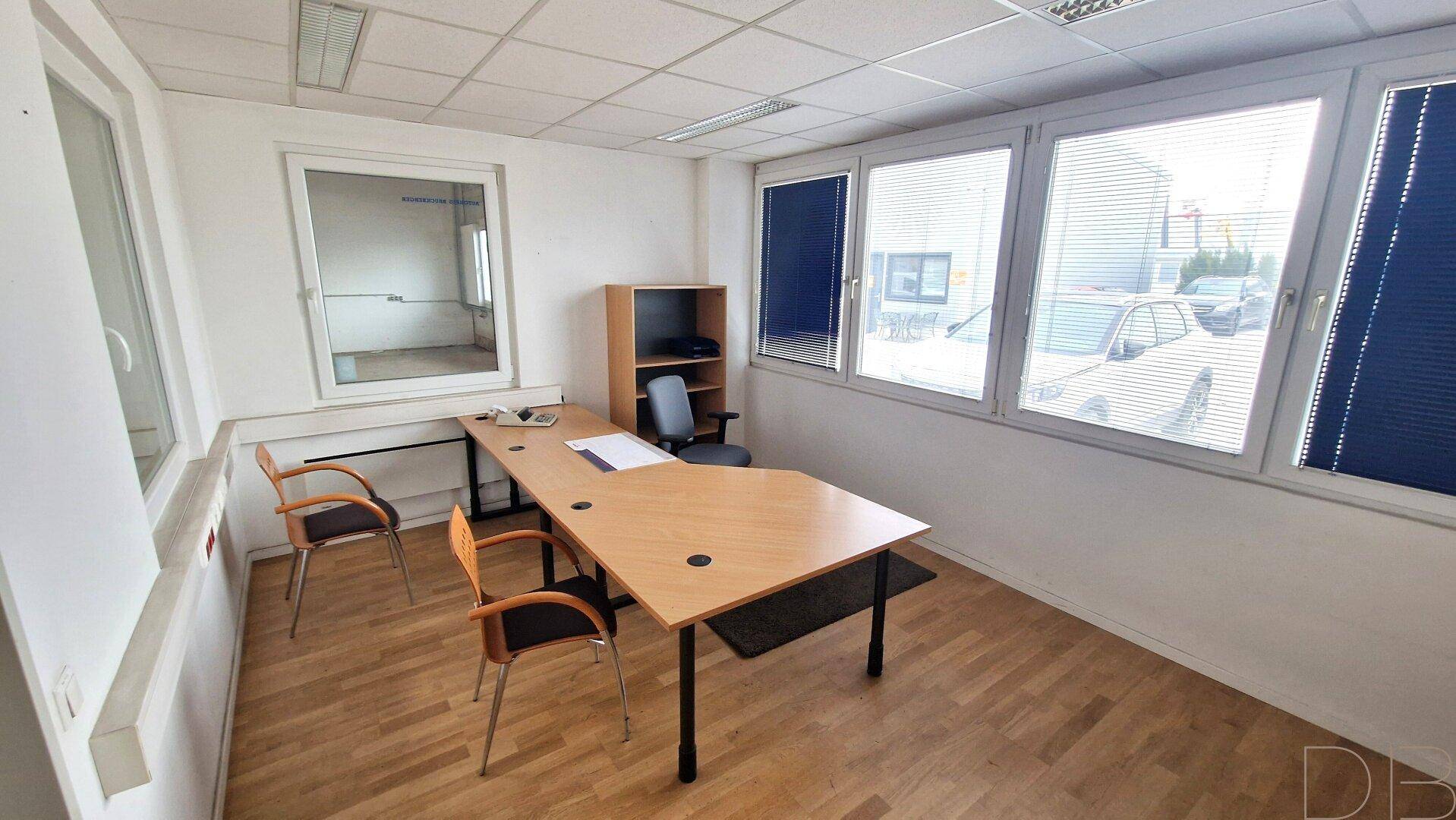 Helles Büro mit Holzfußboden, großen Fenstern und einem Schreibtisch mit Stühlen.