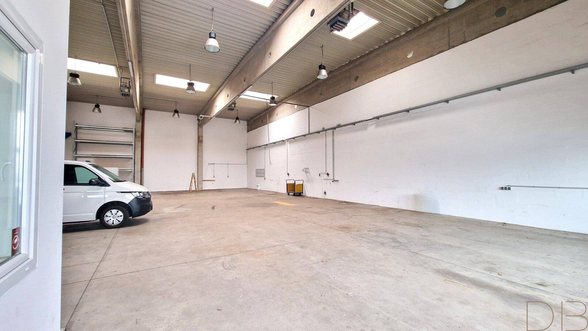 Weitläufige Lagerhalle mit Betonboden, Oberlichtern und einem geparkten Lieferwagen im Vordergrund.