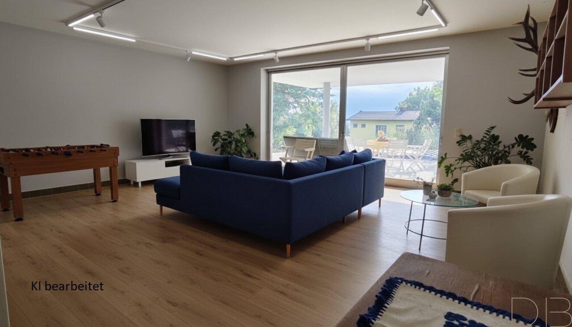 Geräumiger Wohnbereich mit Holzboden, großem Sofa, Tischfußball und Zugang zur Terrasse.