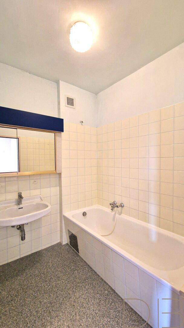 Älteres Badezimmer mit weißen Fliesen, einer Badewanne und einem einzelnen Waschbecken.