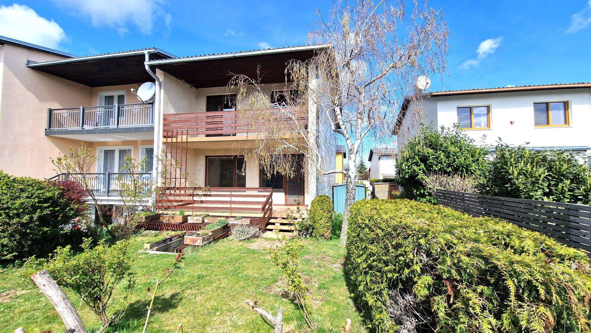 Mehrfamilienhaus mit mehreren Balkonen und einem gepflegten Gartenbereich unter blauem Himmel.