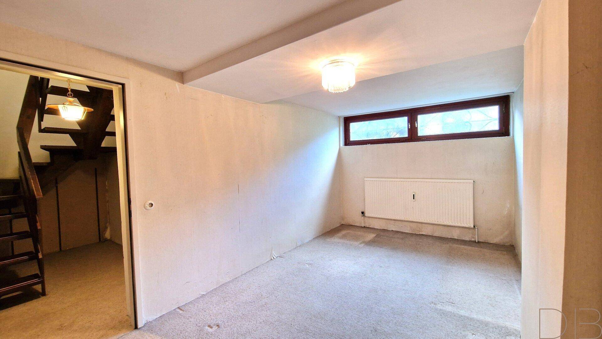 Unfertiger Kellerraum mit kleinem Fenster und Heizkörper, bereit für den Ausbau.