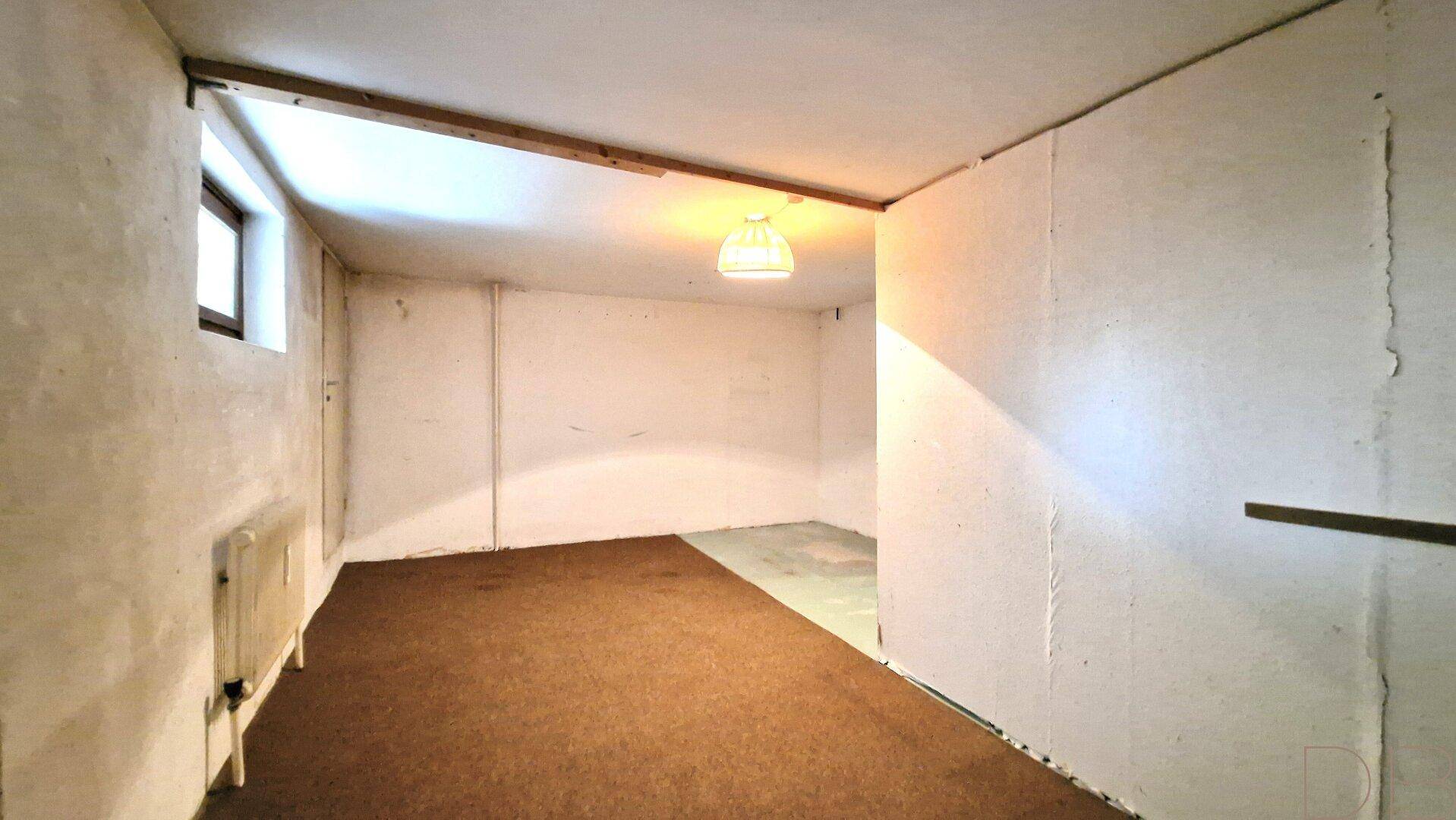 Weiterer Kellerraum mit rauen Wänden, kleinem Fenster und einfacher Beleuchtung.