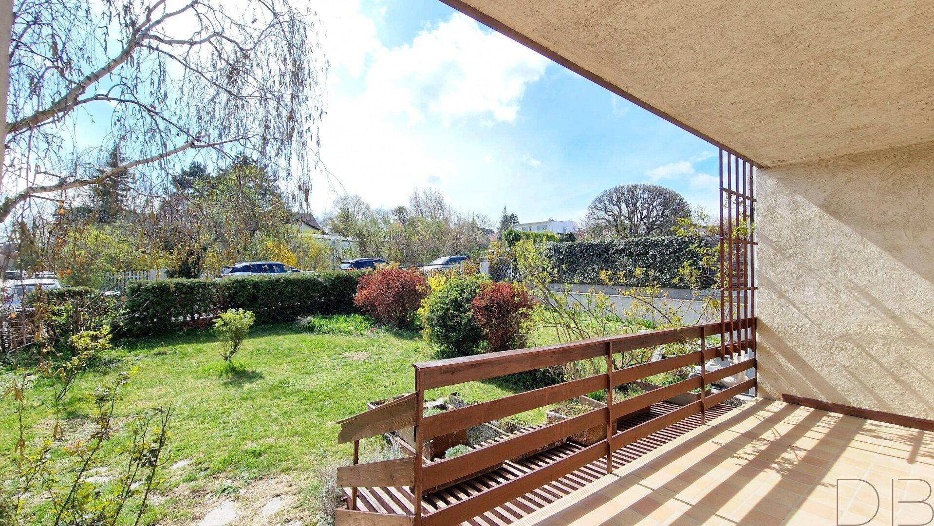 Balkon mit Holzboden und Geländer bietet Blick auf den grünen Garten und die Straße.