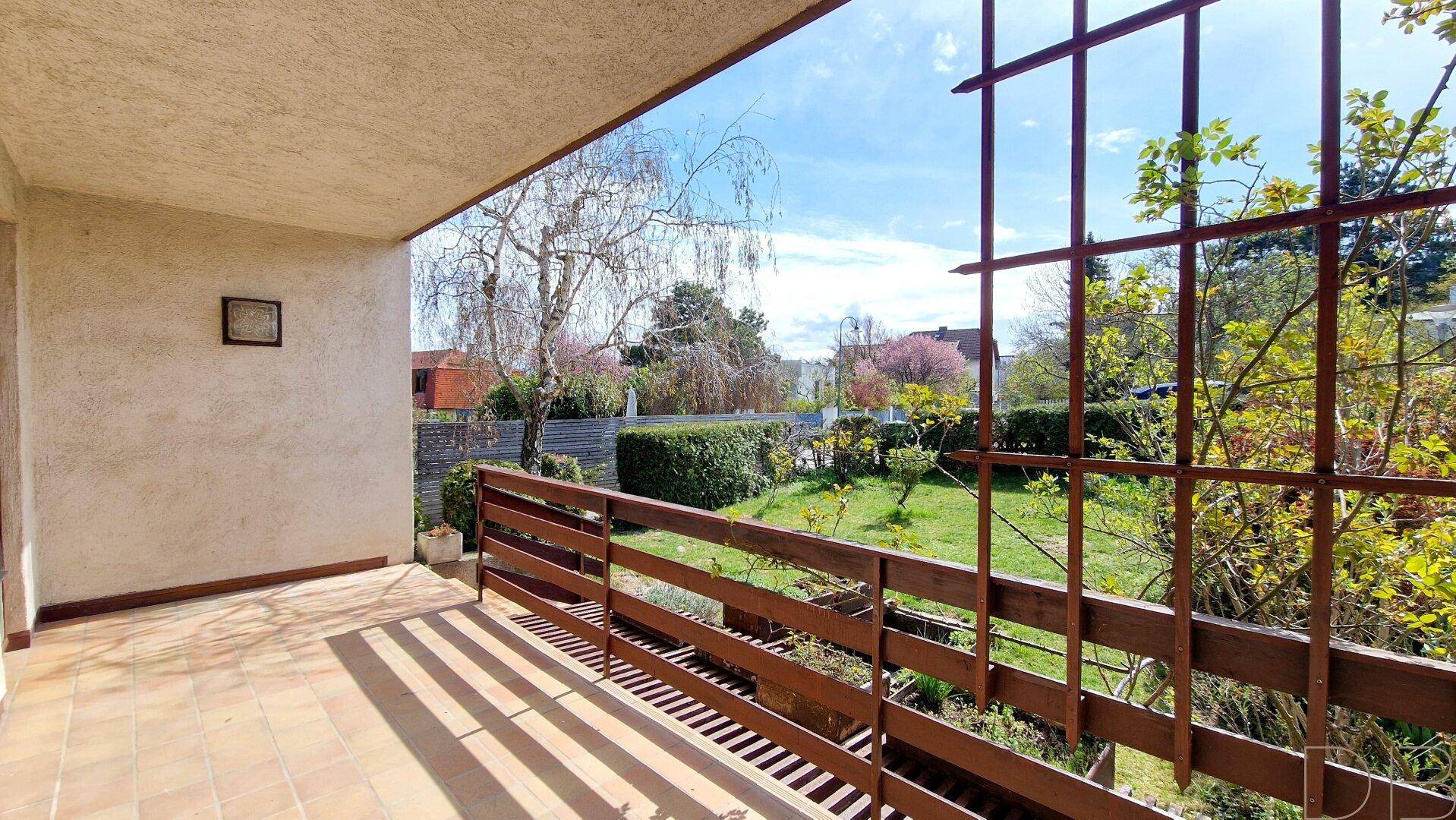 Balkon mit Holzgeländer und Terrakottafliesen, der einen weiten Blick in den Garten bietet.