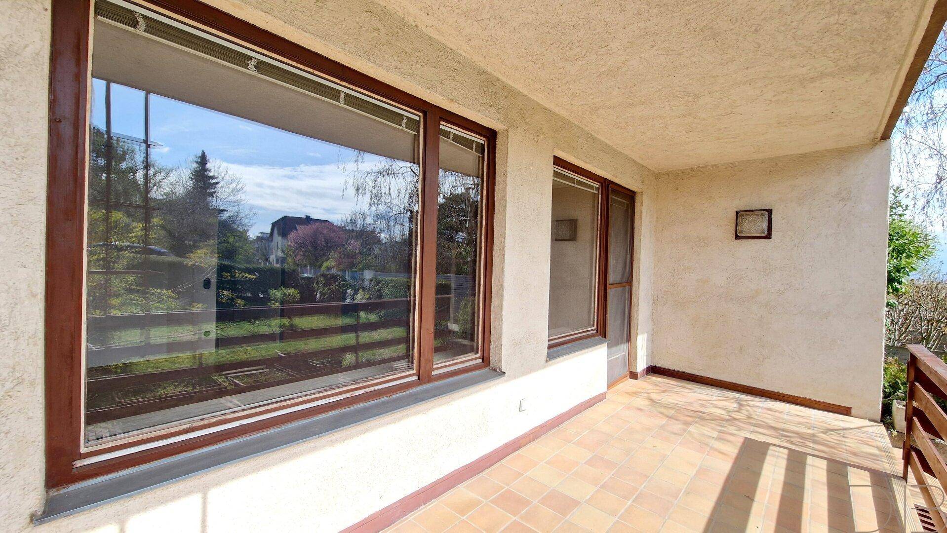 Überdachter Balkon mit Terrakottafliesen und Blick auf den grünen Gartenbereich.