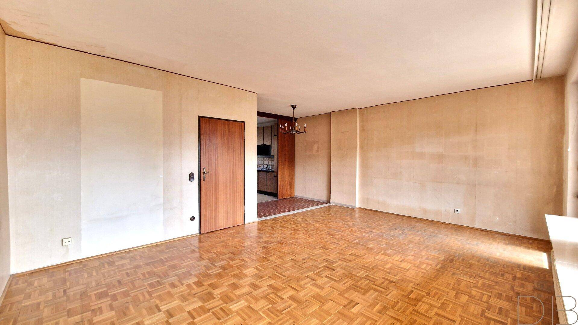 Geräumiges, unmöbliertes Wohnzimmer mit Fischgrätparkett und Zugang zur Küche.