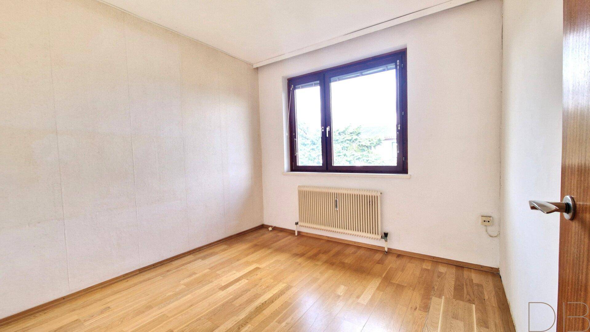Unmöbliertes Schlafzimmer mit Holzboden und einem Fenster, das viel Tageslicht hereinlässt.