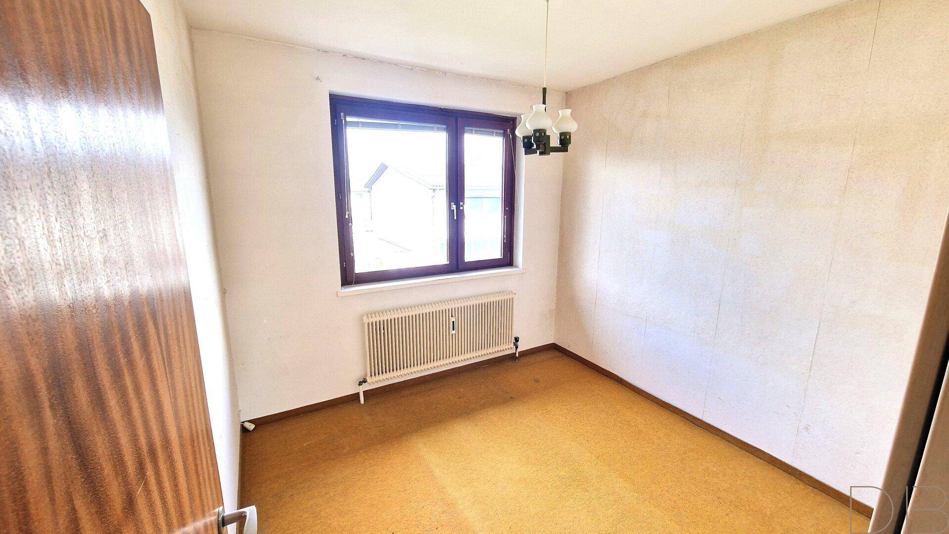 Unmöbliertes Zimmer mit gelbem Bodenbelag und einem Fenster, das Tageslicht spendet.