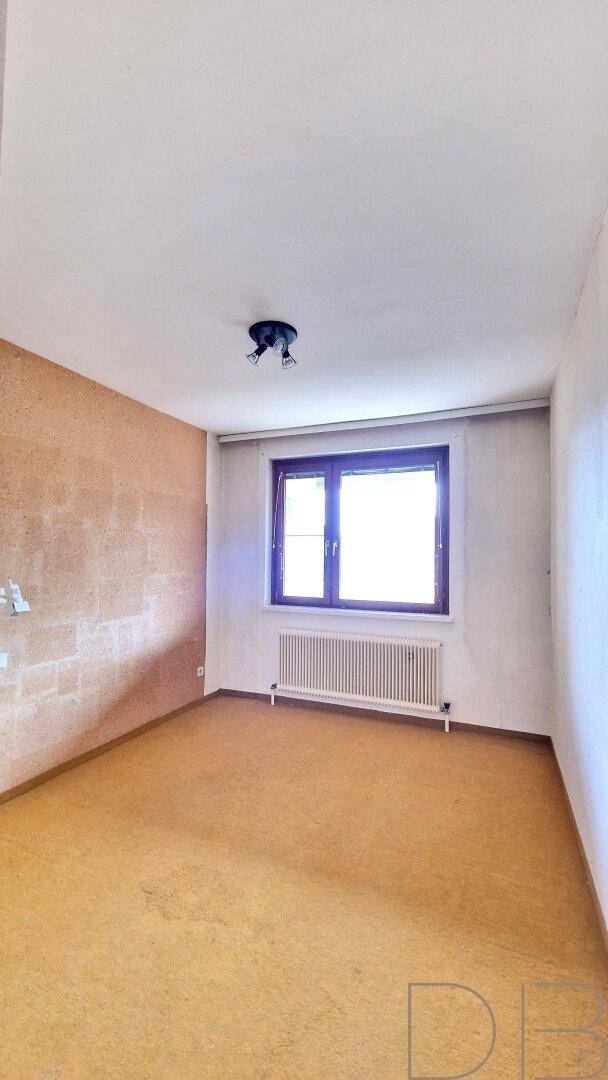 Helles, unmöbliertes Zimmer mit gelbem Bodenbelag und einem großen Fenster.