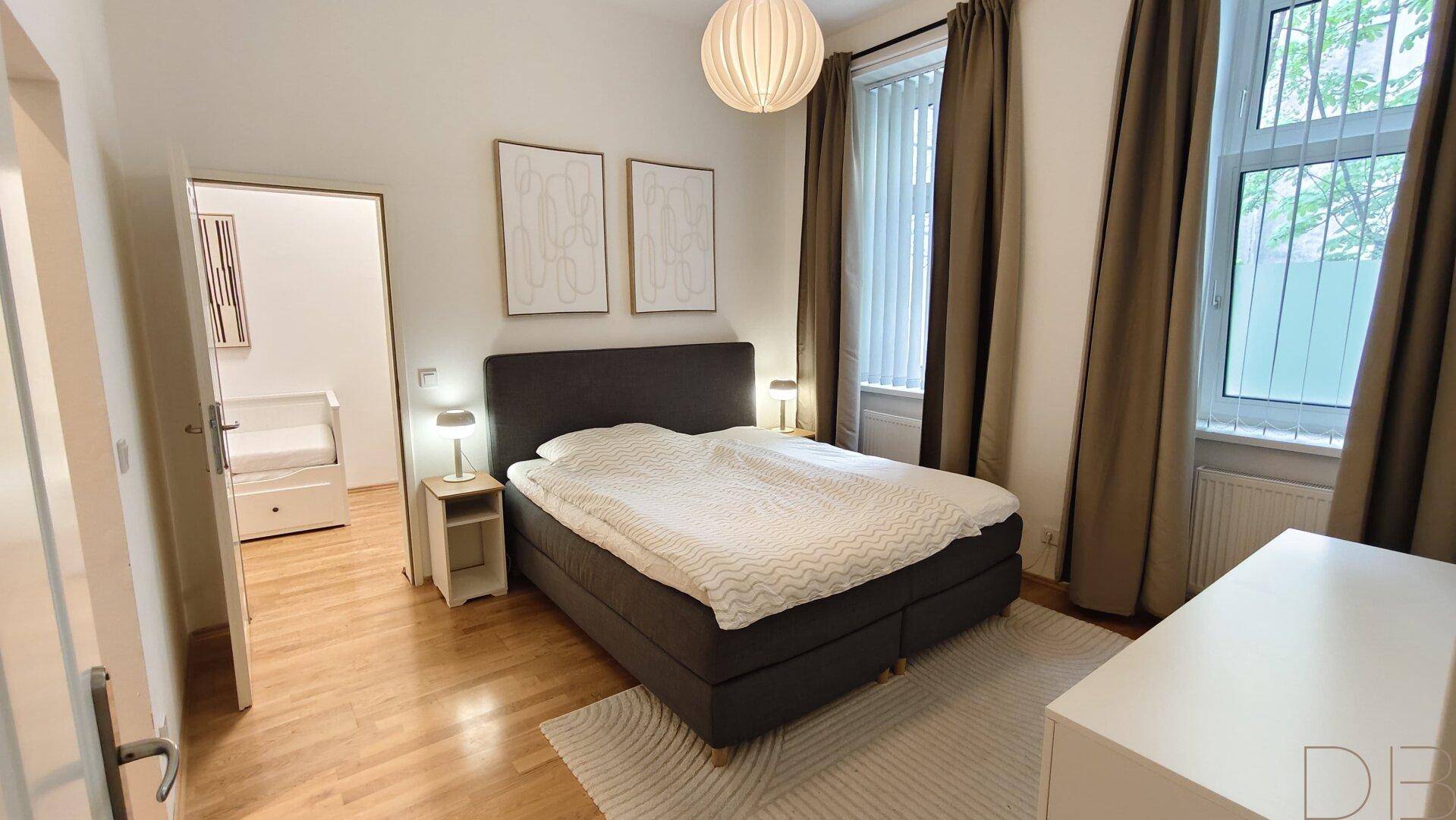 Gemütliches Schlafzimmer mit Doppelbett, Parkettboden und großen Fenstern.