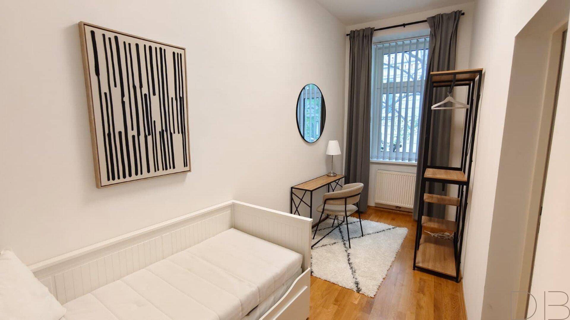 Helles Zimmer mit Einzelbett, Schreibtisch und modernem Kleiderständer.