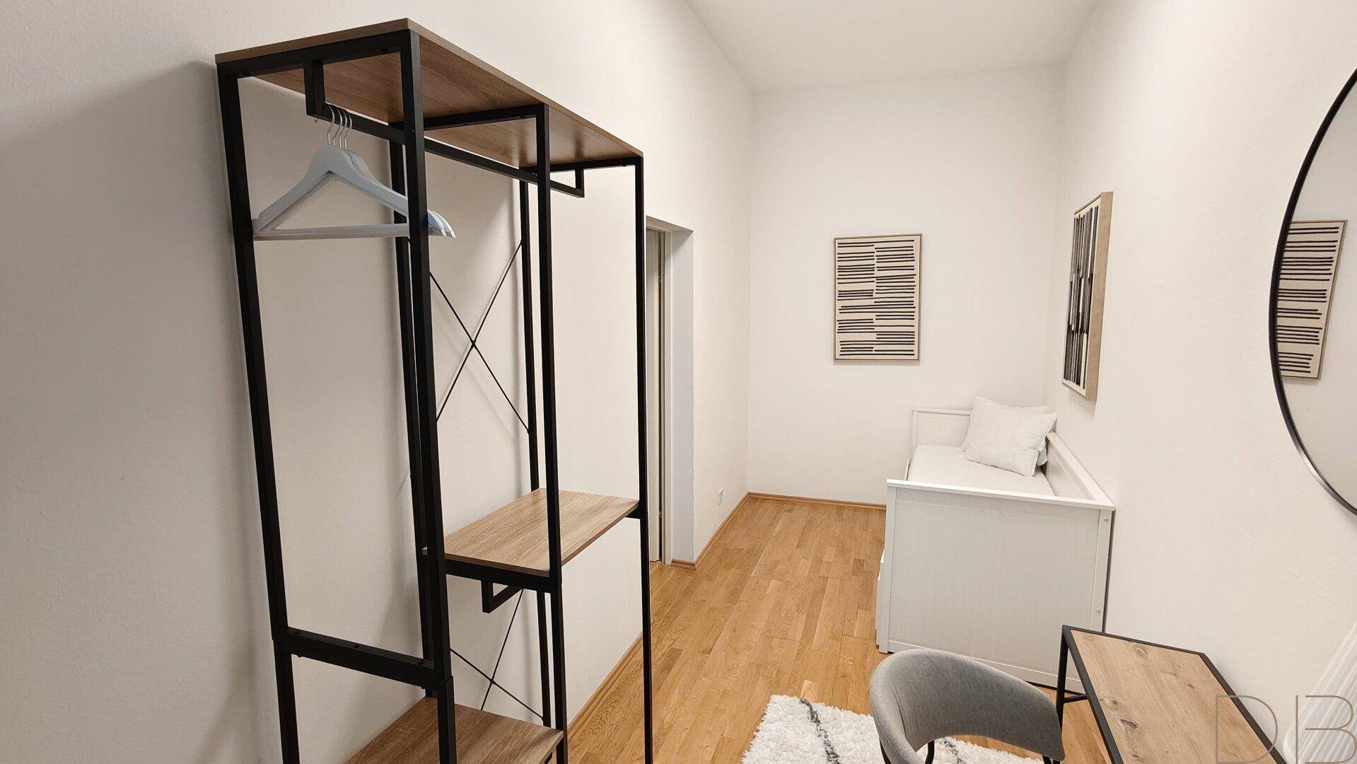 Modern eingerichtetes Zimmer mit Einzelbett, Spiegel und offenem Kleiderständer.