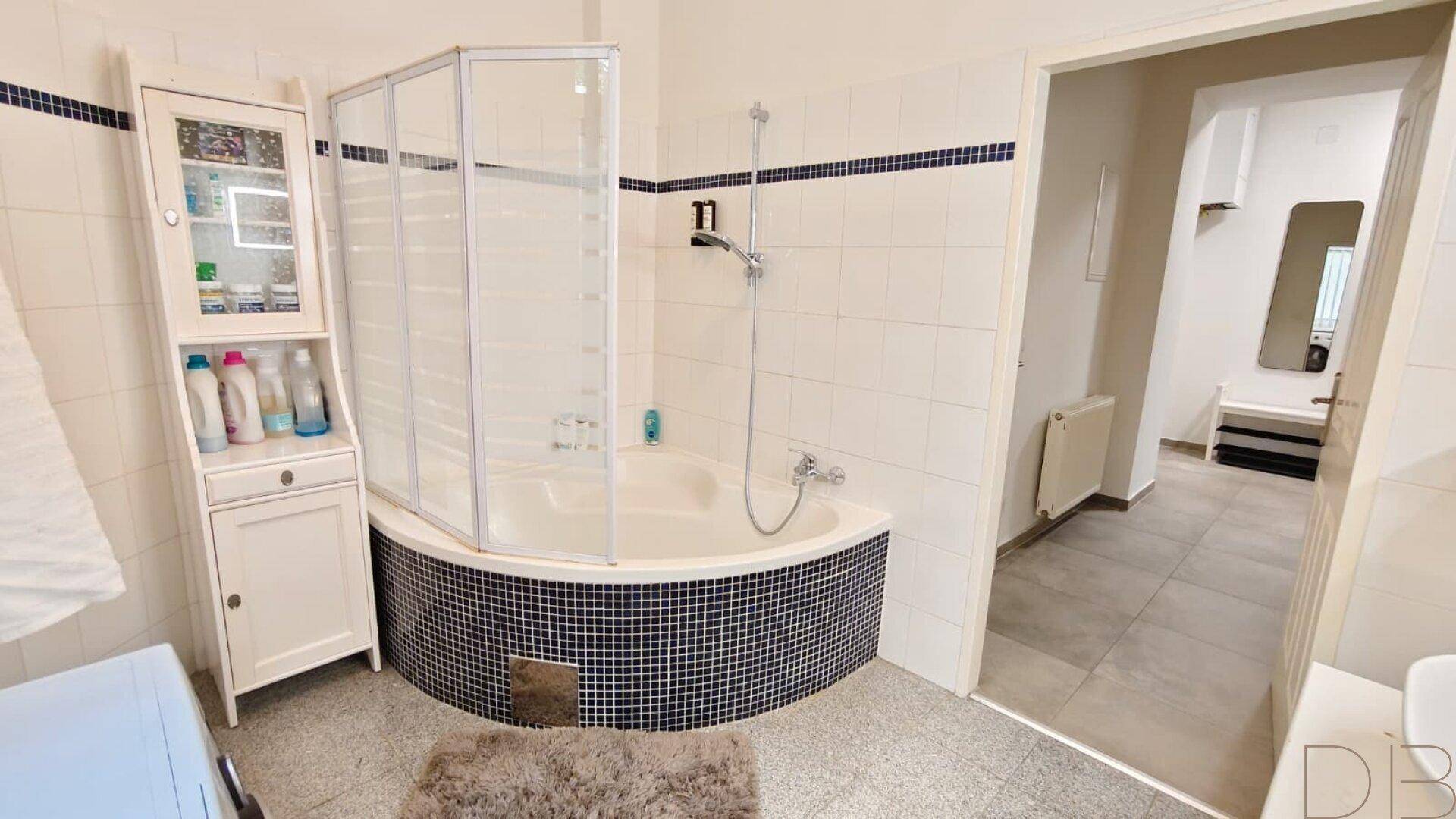 Badezimmer mit Eckbadewanne, Duschabtrennung und weiß-blauen Fliesen.
