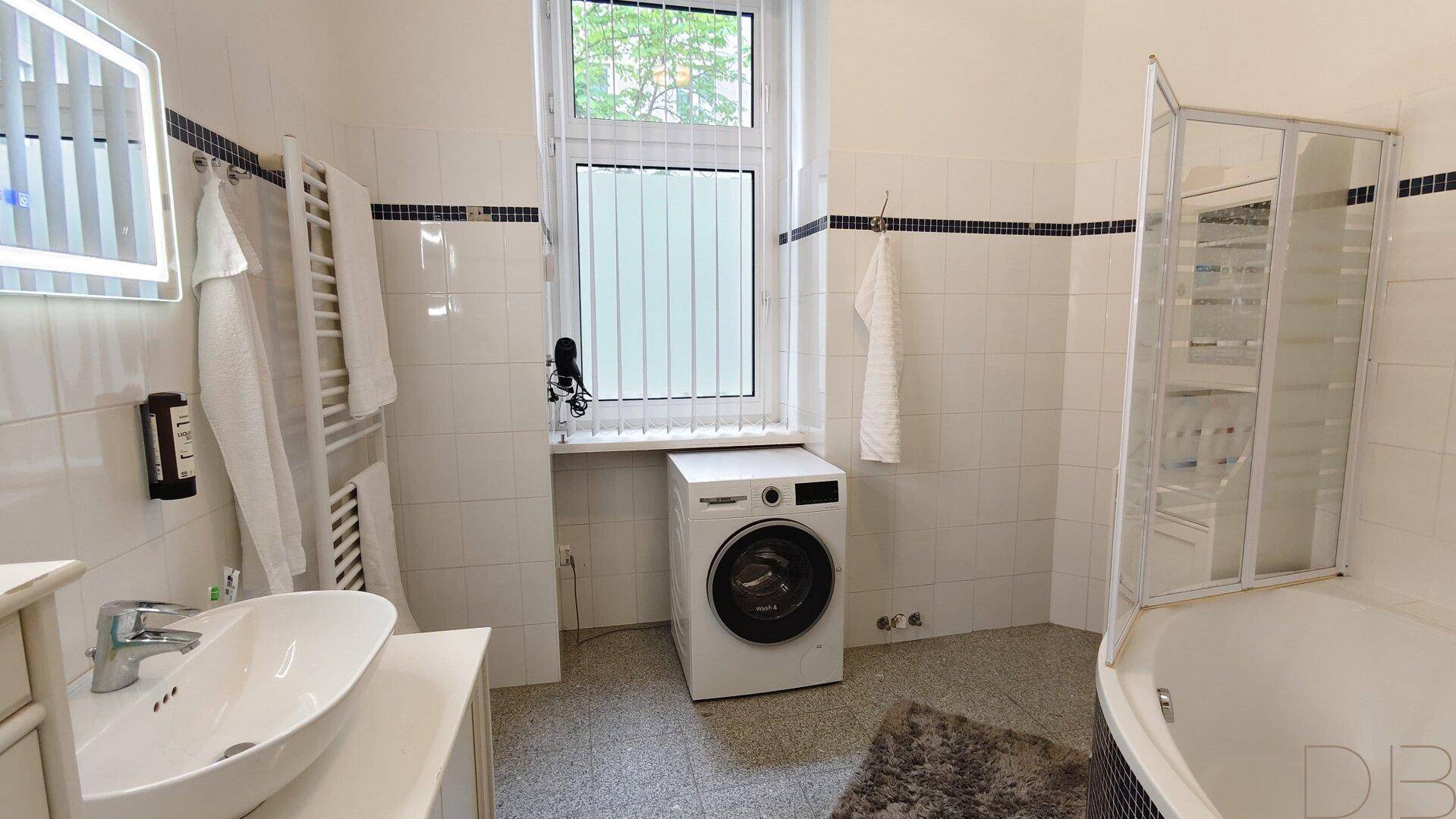Helles Badezimmer mit Fenster, Waschmaschine, Waschbecken und beheiztem Handtuchhalter.