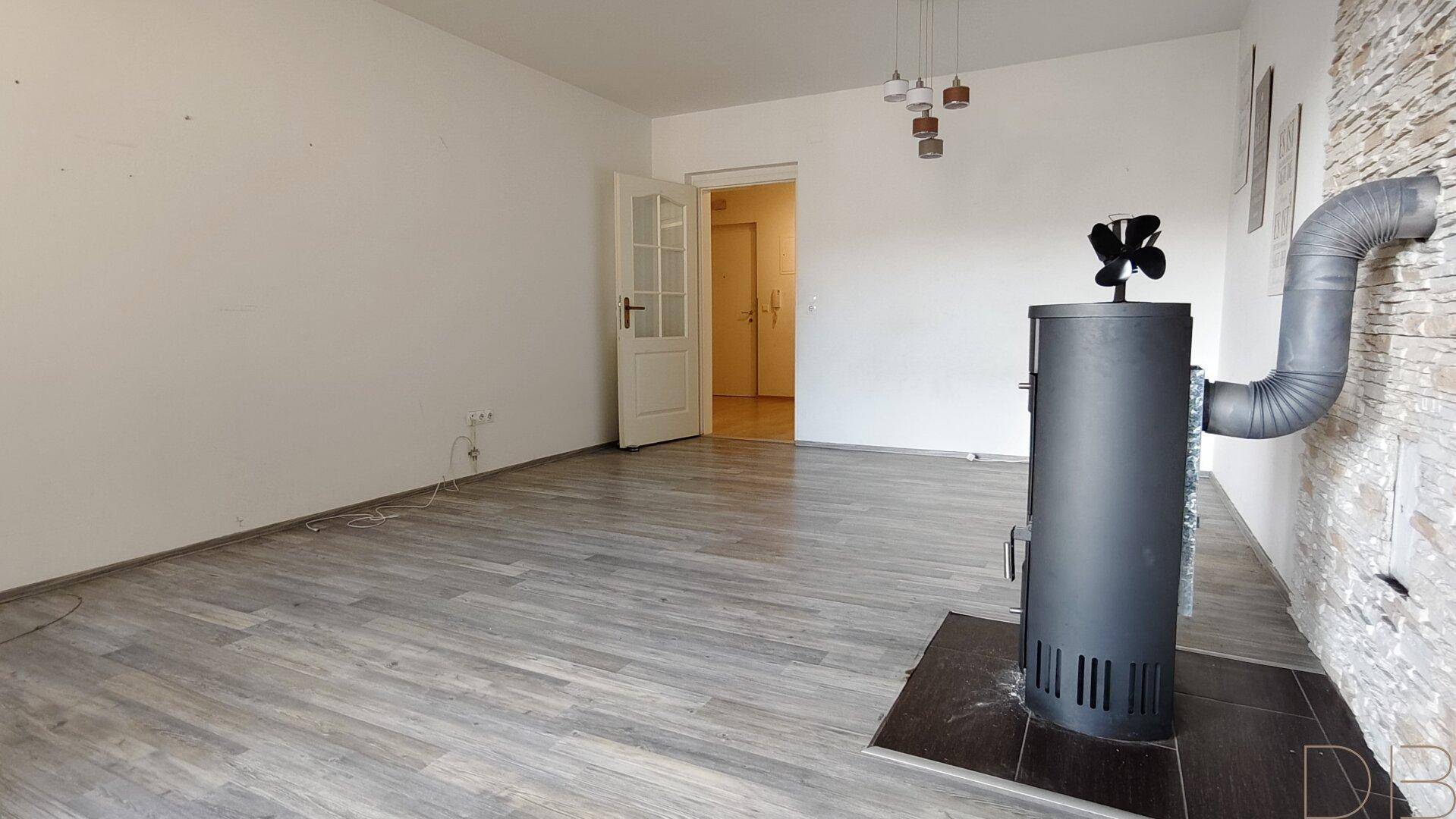 Leeres Wohnzimmer mit Kaminofen, Laminatboden und weiß gestrichenen Wänden, bereit zur Einrichtung.
