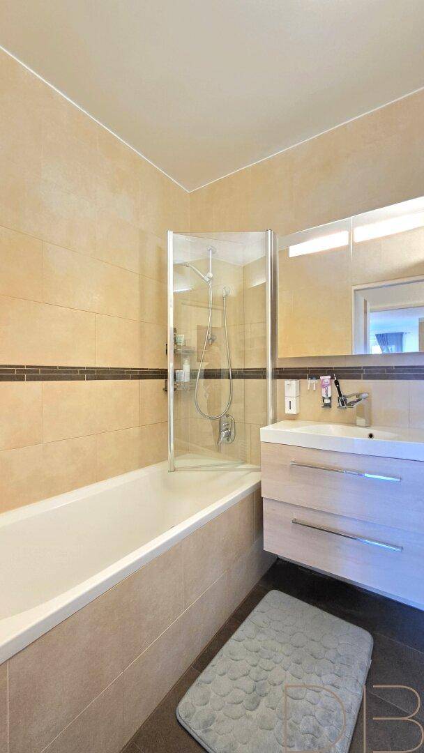 Modernes Badezimmer mit Badewanne, Duschabtrennung, Waschbecken und beigefarbenen Wandfliesen.