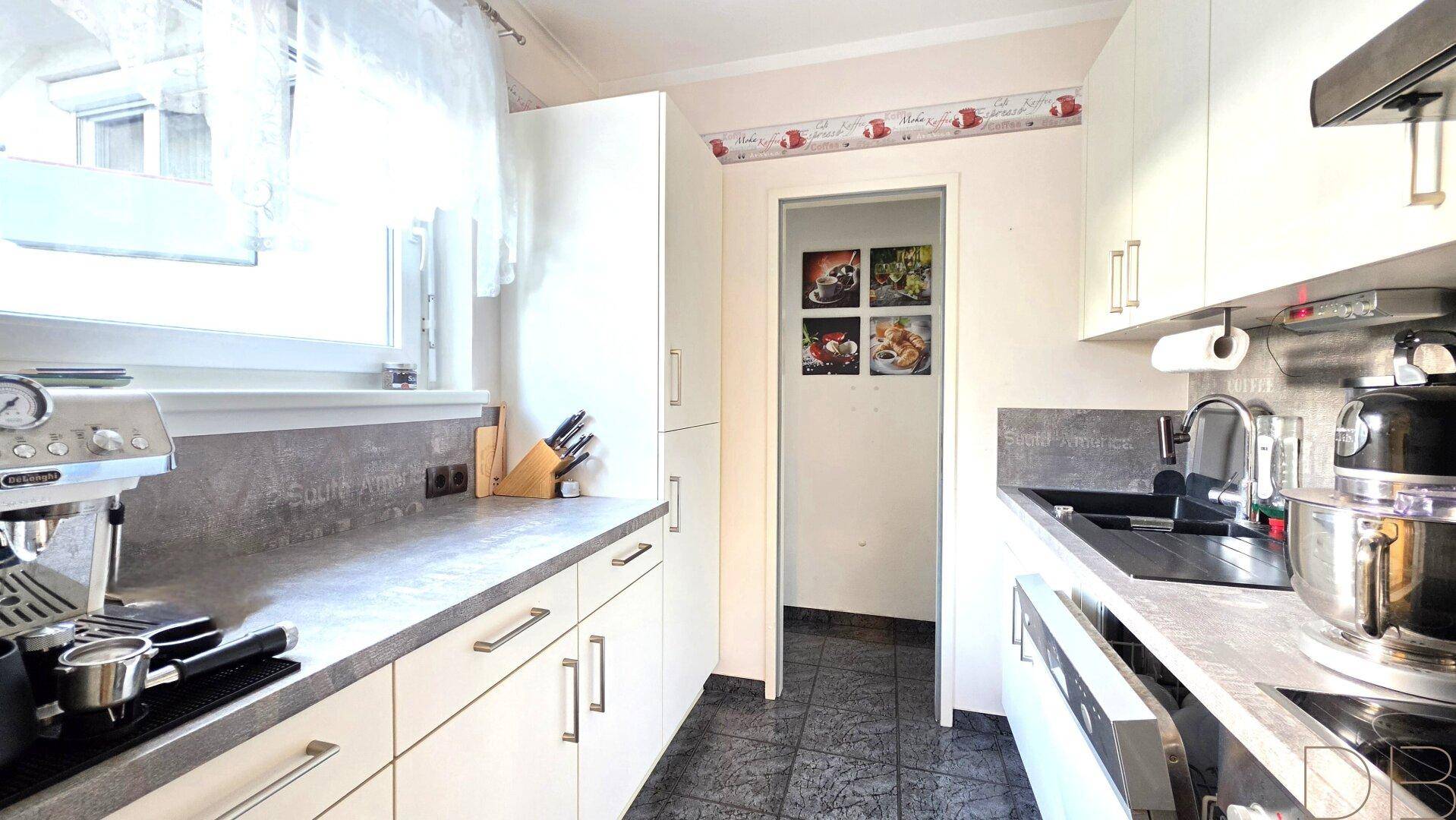 Funktionale Küche mit weißen Schränken, grauen Arbeitsplatten und dunklem Fliesenboden.